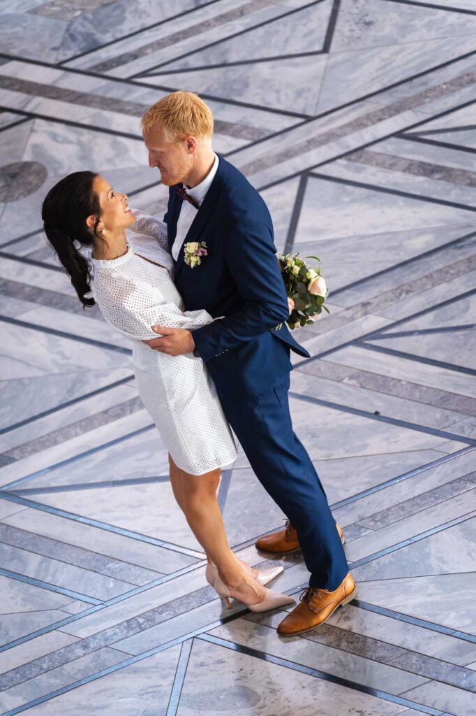 Brudepar som holder rundt hverandre i den store hallen, fotografert ovenfra trappen.