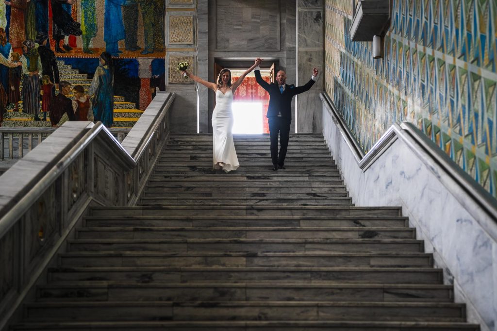 Brudeparet strekker armene i været mens de går ned trappene i Oslo rådhus.