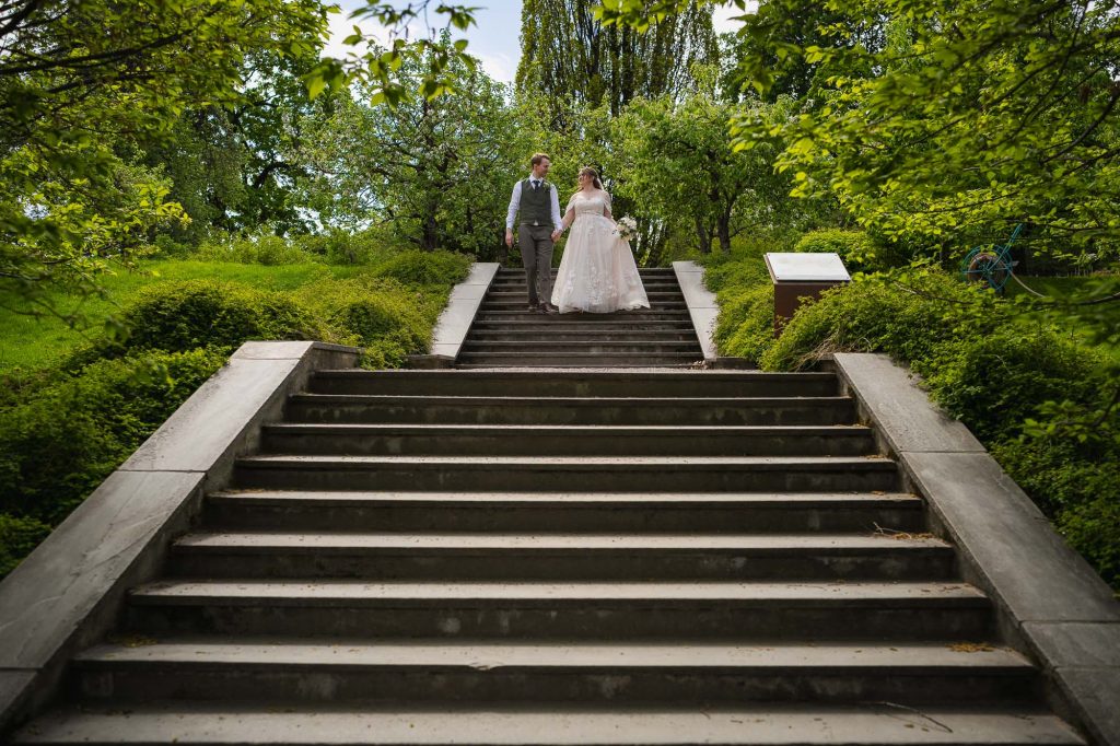 Brudeparet går hånd i hånd ned trappen i botanisk hage i Oslo.