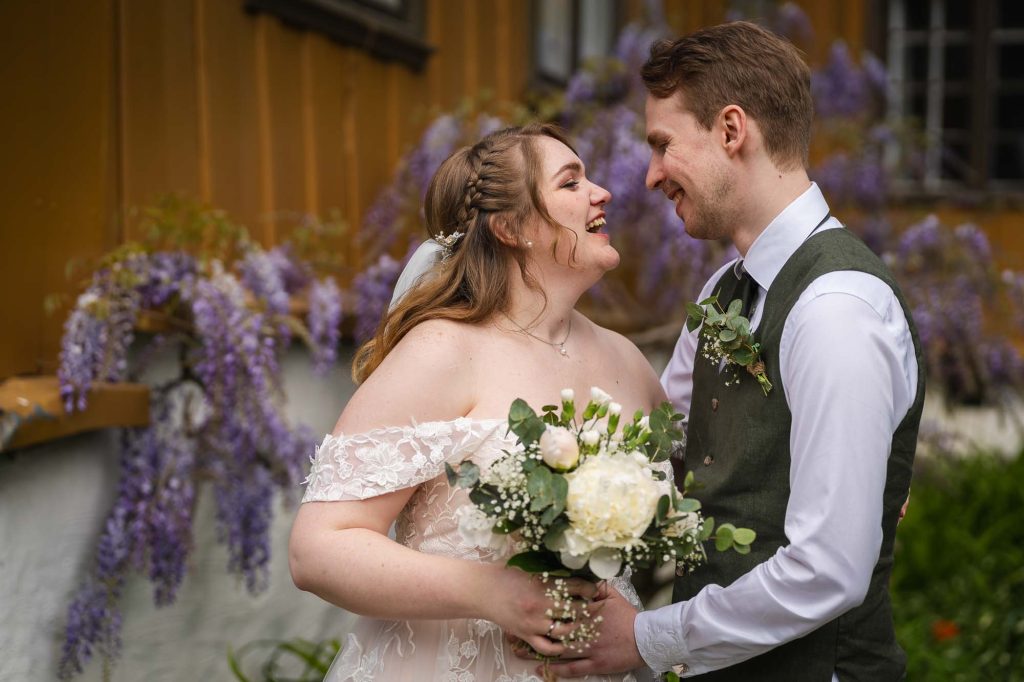 Brudeparet koser seg med hverandre foran vakre violette blomster i Botanisk hage i Oslo.