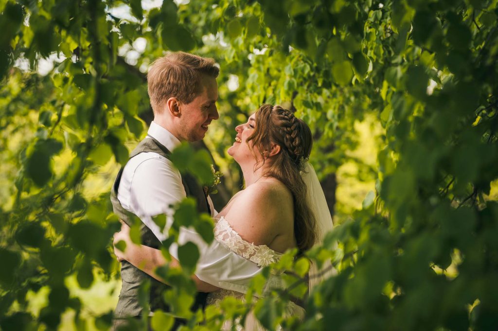 Brudeparet koser seg med hverandre bak løvverket i botanisk hage i Oslo.