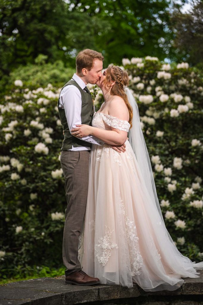 Brudeparet kysser hverandre med hvite blomster som bakgrunn.