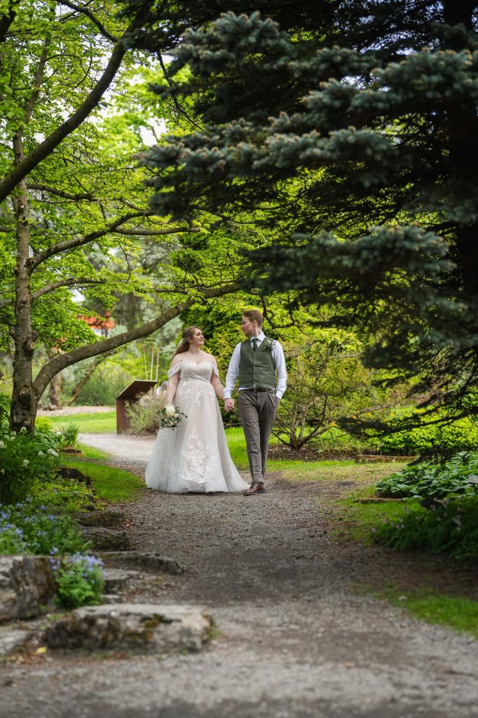 Brudeparet går hånd i hånd på stien i botanisk hage i Oslo.