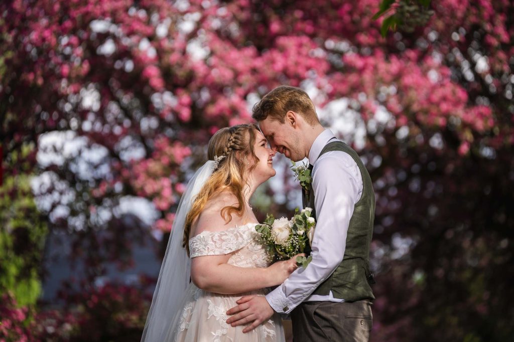 Brudeparet holder om hverandre foran vakre røde blomster i Botanisk hage i Oslo.