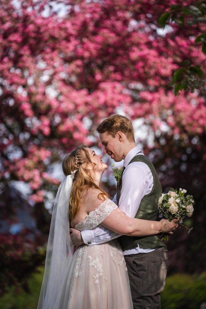Brudeparet holder om hverandre foran vakre røde blomster i Botanisk hage i Oslo.