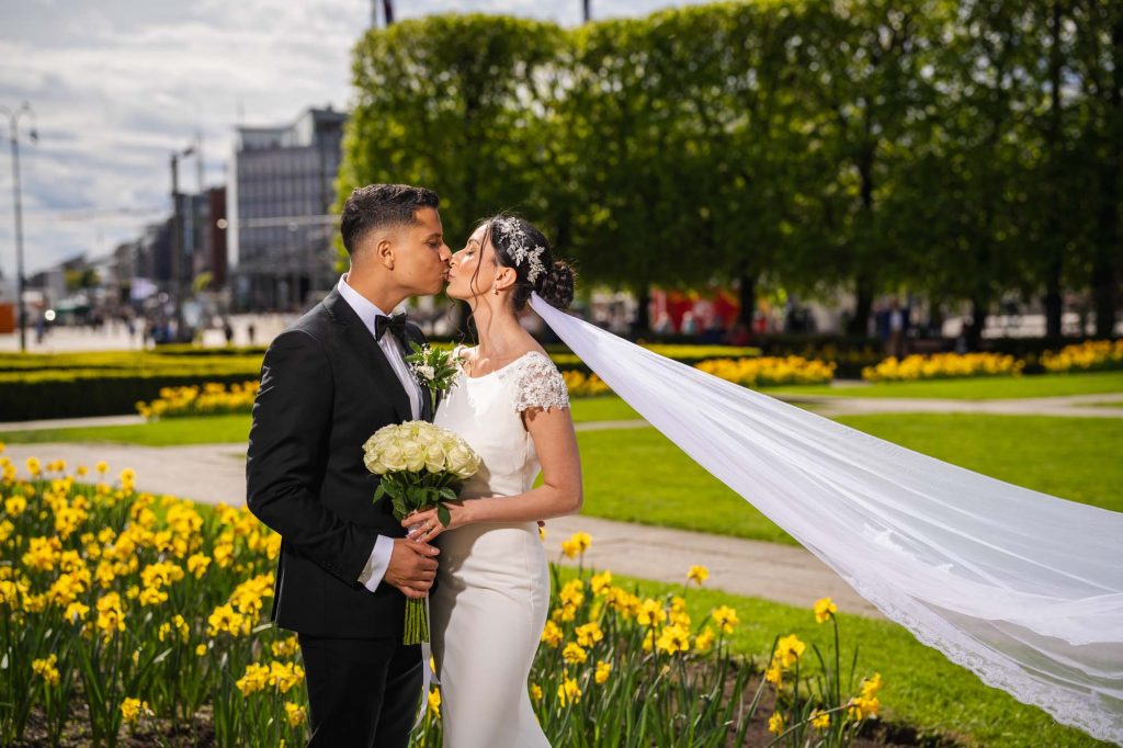 Bruden og brudgommen kysser hverandre blant blomstene i hagen utenfor Oslo rådhus.