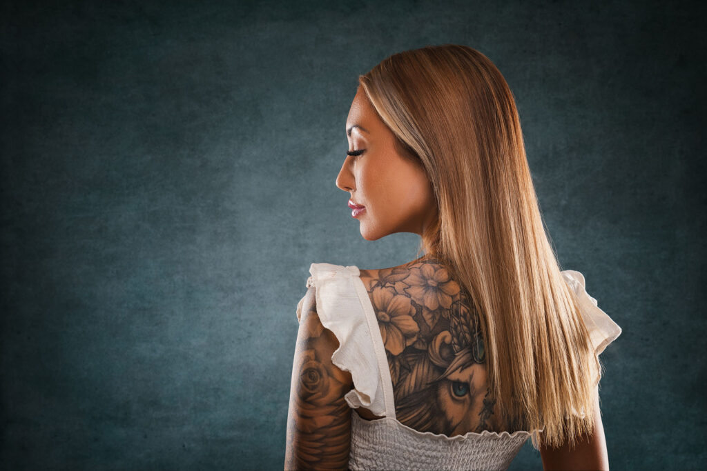 Et vakkert portrett av en kvinne i profil som viser frem en detaljert tatovering på ryggen, tatt i fotostudio.