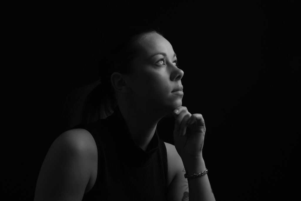 Et stemningsfullt sort-hvitt-portrett av en kvinne i profil, fotografert med lavmælt lyssetting som skaper dype skygger og en rolig atmosfære.