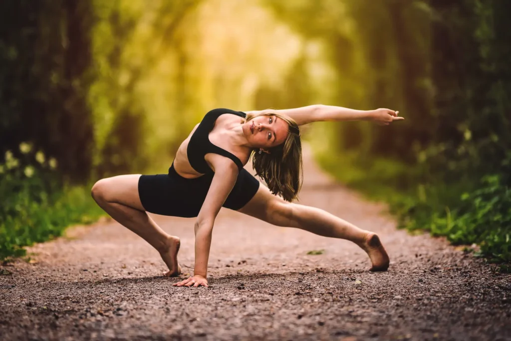 En kvinne i en dynamisk og fleksibel yogaposisjon på en sti i skogen, fotografert av en livsstilsfotograf med varmt naturlig lys.